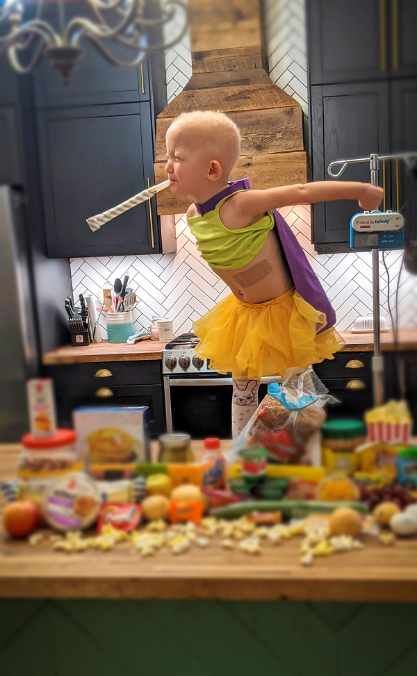 Child stands on a table blowing a noisemaker.