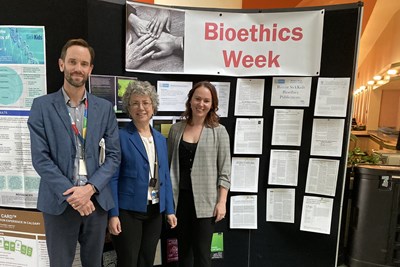 Three people stand together in front of an academic poster presentation.