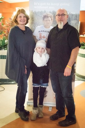 Two adults stand arm in arm with a child standing in between them.