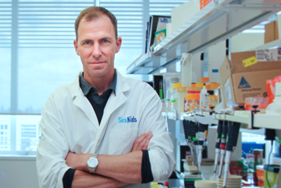 Peter Dirks standing against a laboratory bench, surrounded by lab equipment