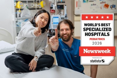 Youth and doctor sit together in a clinical setting, holding up their pointer fingers.
