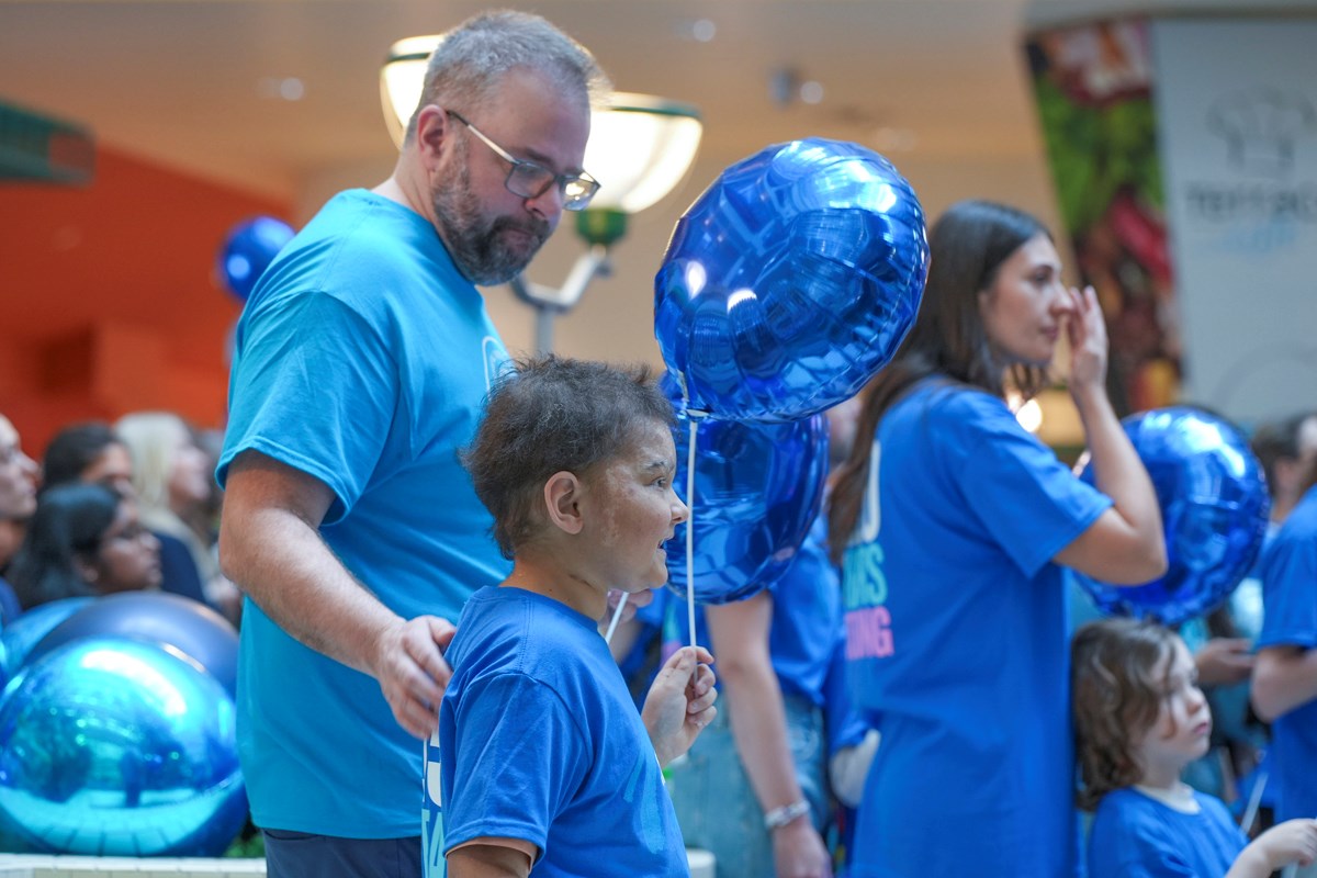 A father and child dressed in blue SickKids t-shirts. The child is holding a blue balloon.