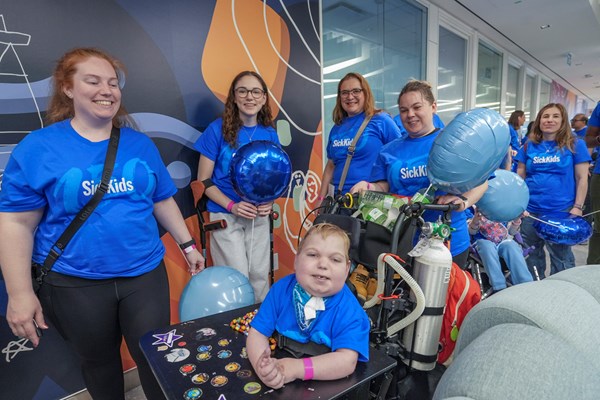 A group of SickKids 150 parade participants smiling and dressed in blue SickKids 150 t-shirts and holding blue balloons.